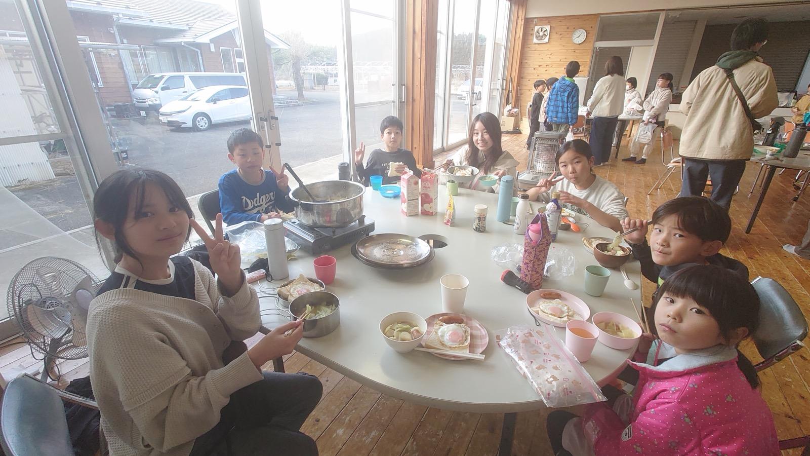 大きな丸テーブルを囲んで、子どもたちが朝ごはんを食べている。目玉焼き、スープ、パン、ジュースが並ぶ
