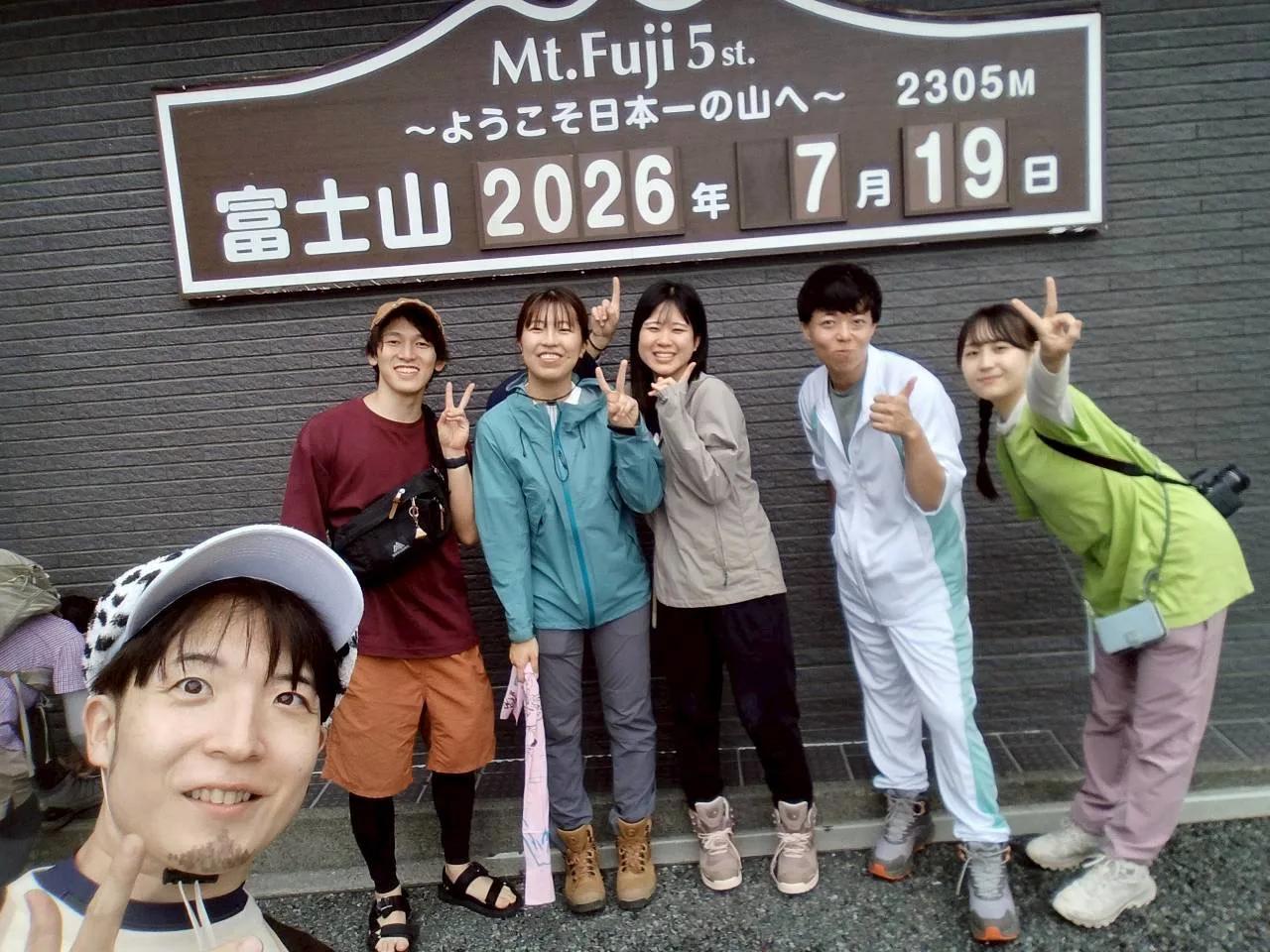 「富士山 2026年7月19日 2305M」の看板の前に並ぶメンバー