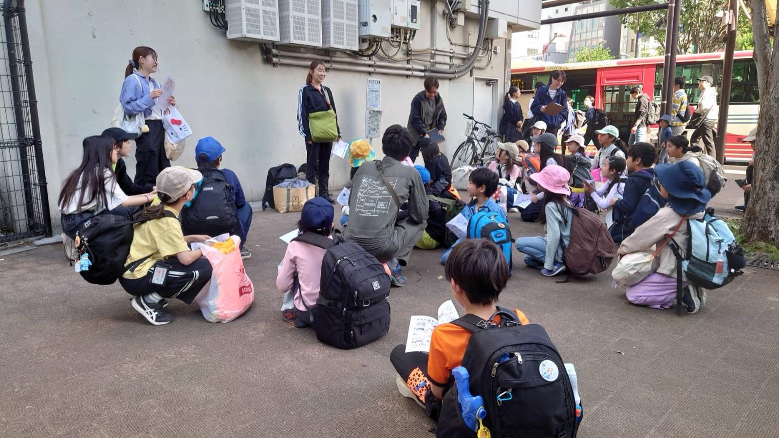 荻窪駅北口広場。しおりを受け取って地面に座り、出発前の説明を聞く