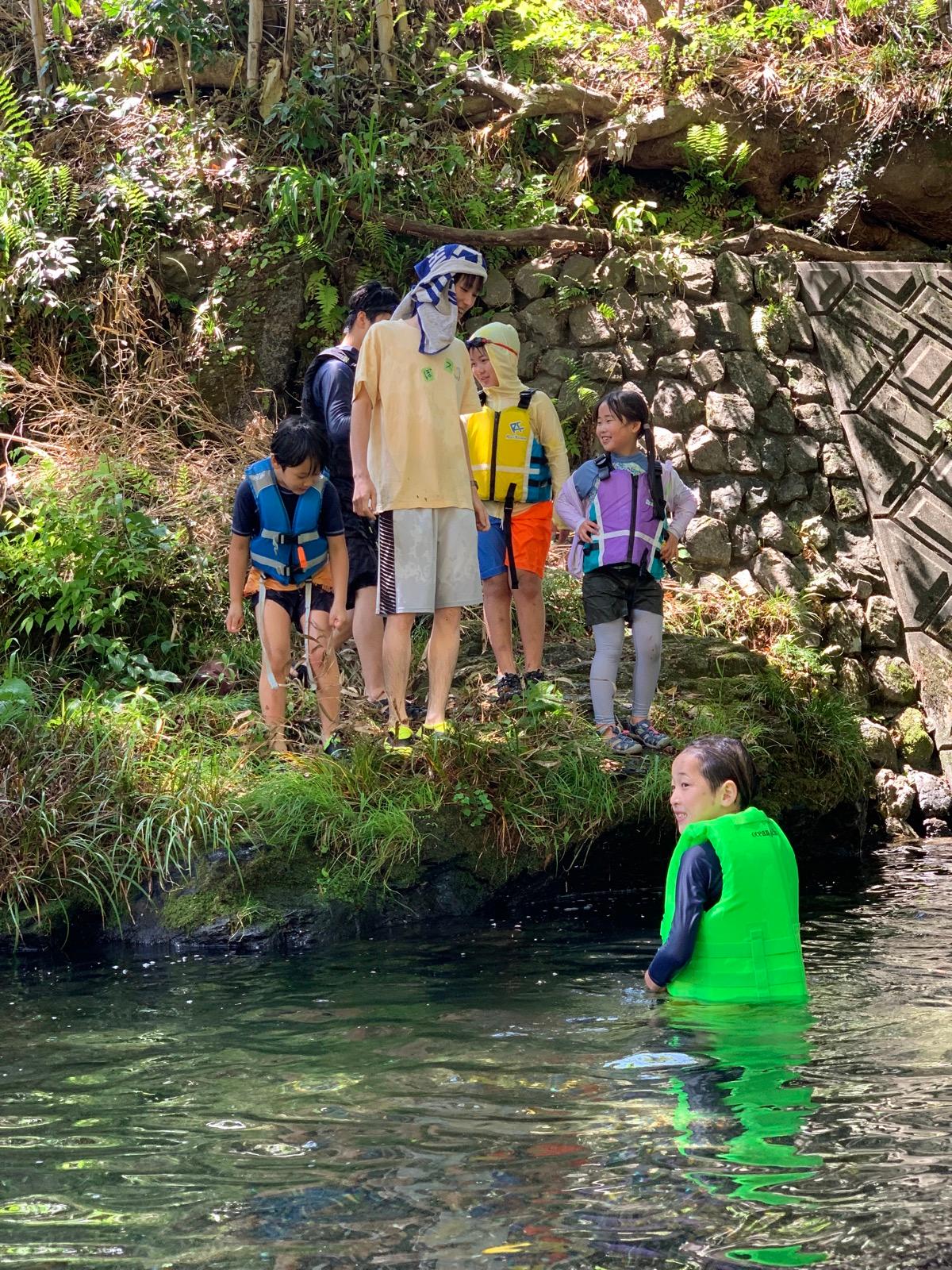 深みで胸まで水に浸かり、岸の仲間のほうを振り返る子ども