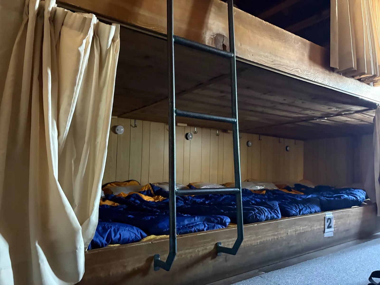 山小屋の二段式ドミトリーに青い寝袋がずらりと並ぶ様子