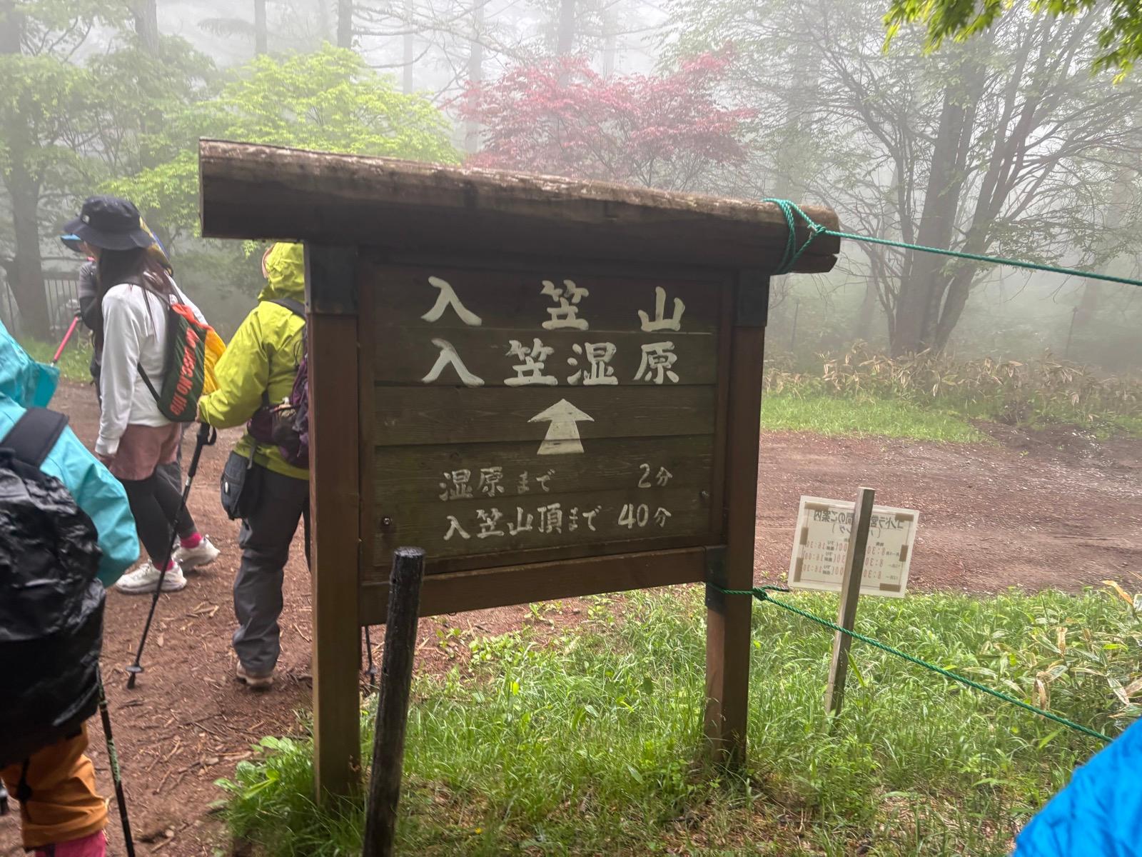 登山道の道標。「入笠山登山口」「入笠山頂まで40分」「湿原まで2分」と書かれた木の標識が霧の中に立っている