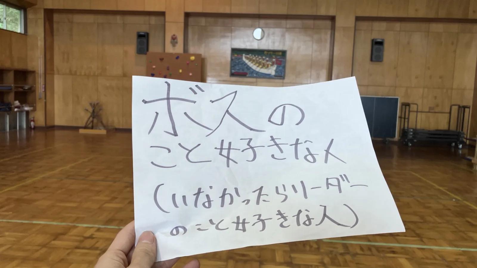 広間で、手に持たれた紙に「ボスのこと好きな人（いなかったらリーダーのこと好きな人）」と手書きされている