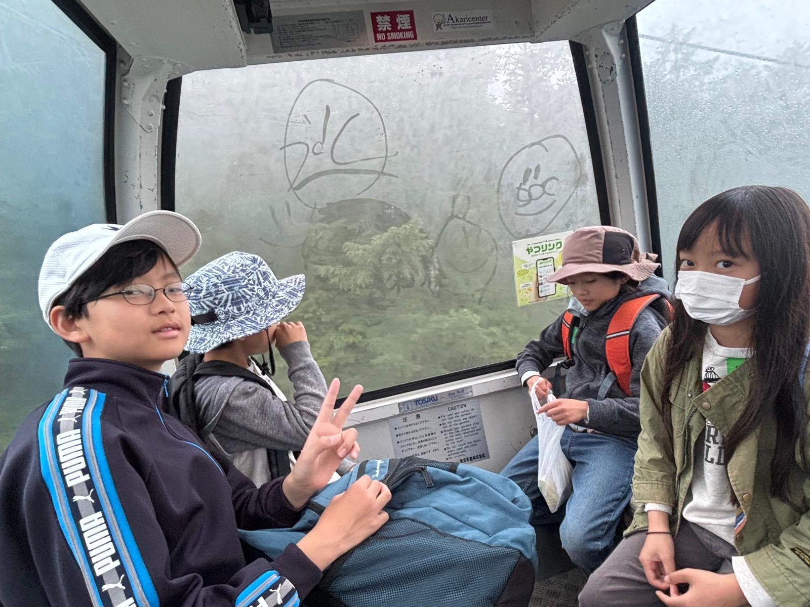 ゴンドラの車内から。曇った窓ガラスに指で顔の落書きが描かれている。窓の外は白い霧