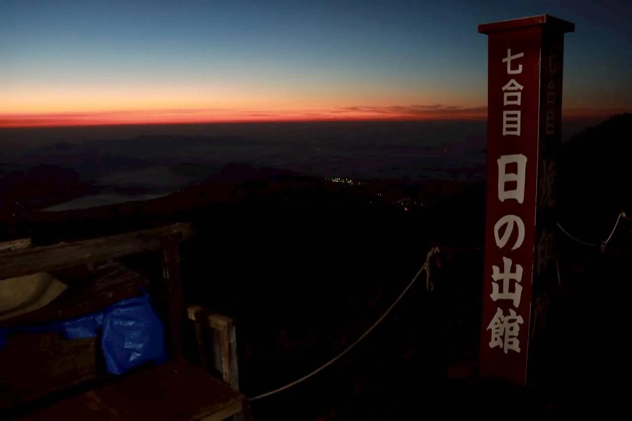 夕暮れの茜色の空を背にした「七合目 日の出館」の標柱