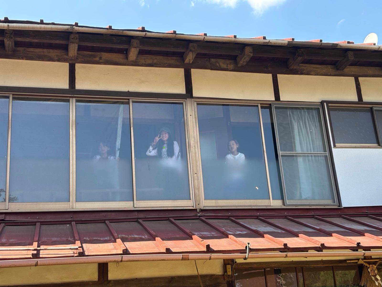 古民家の2階の窓。3人が中から手を振っている