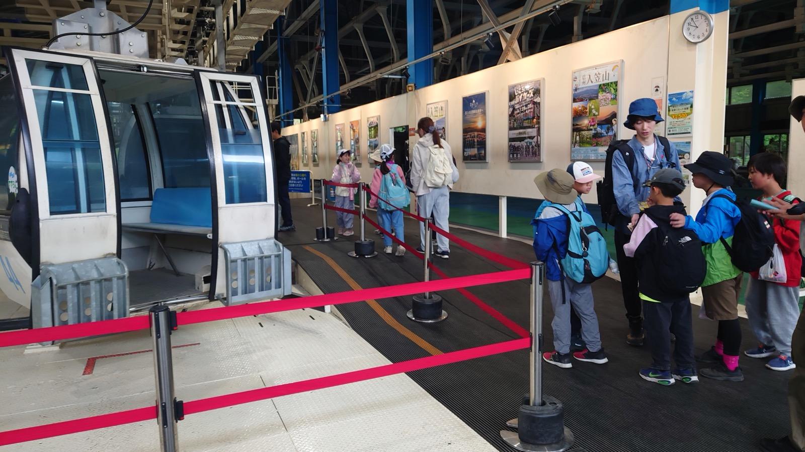 ゴンドラ乗り場。停まったゴンドラの前で、リュックを背負った子どもたちが順番を待って並んでいる