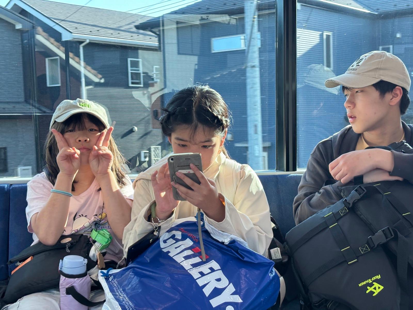 帰りの電車の座席。窓から西日が差し込むなか、3人が並んで座っている