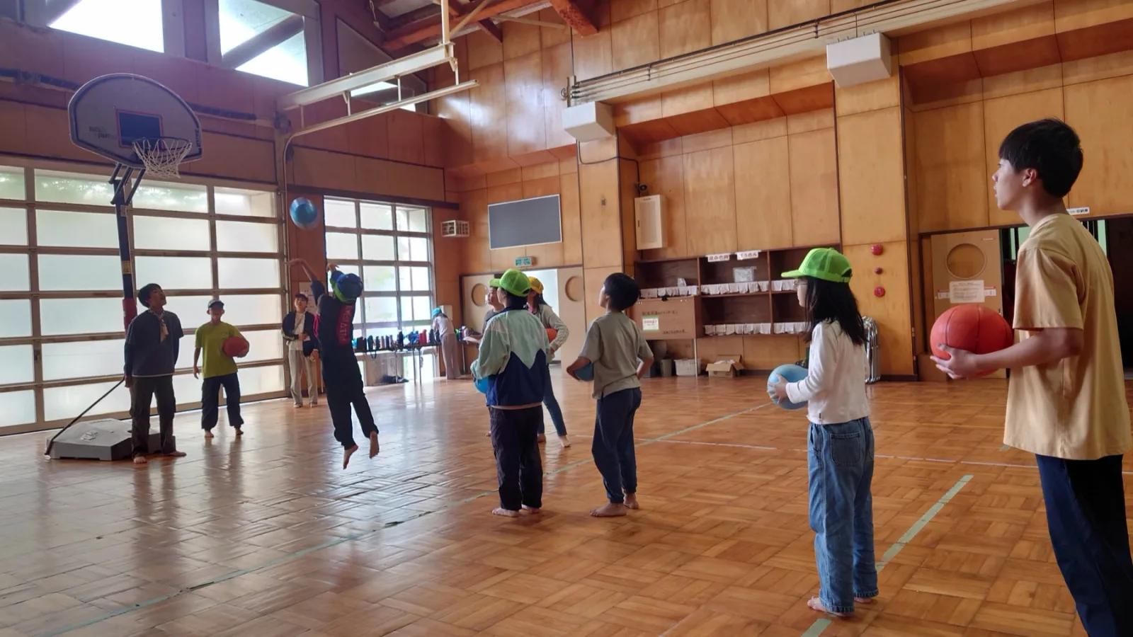体育館全体。参加者たちが散らばってボールを投げ合っている。手前でボールを持って立つ人、跳び上がっている人がいる