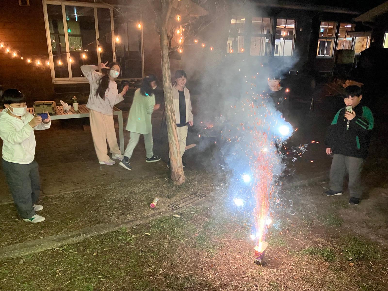 夜の中庭で、噴出花火が火花を高く噴き上げている。少し離れて子どもたちが見ている