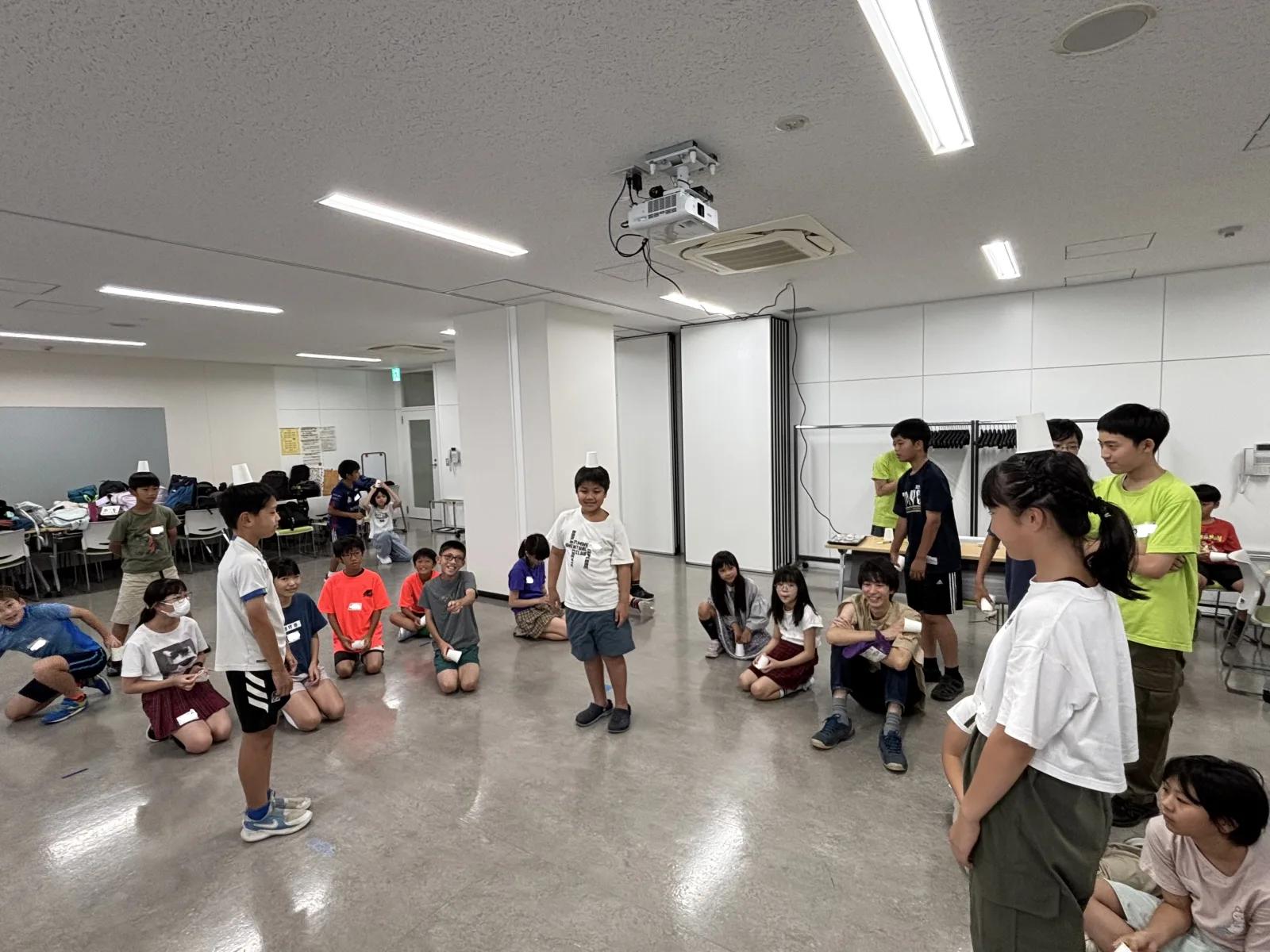 会議室いっぱいに広がった子どもたちが、それぞれ頭の上に紙コップを乗せている