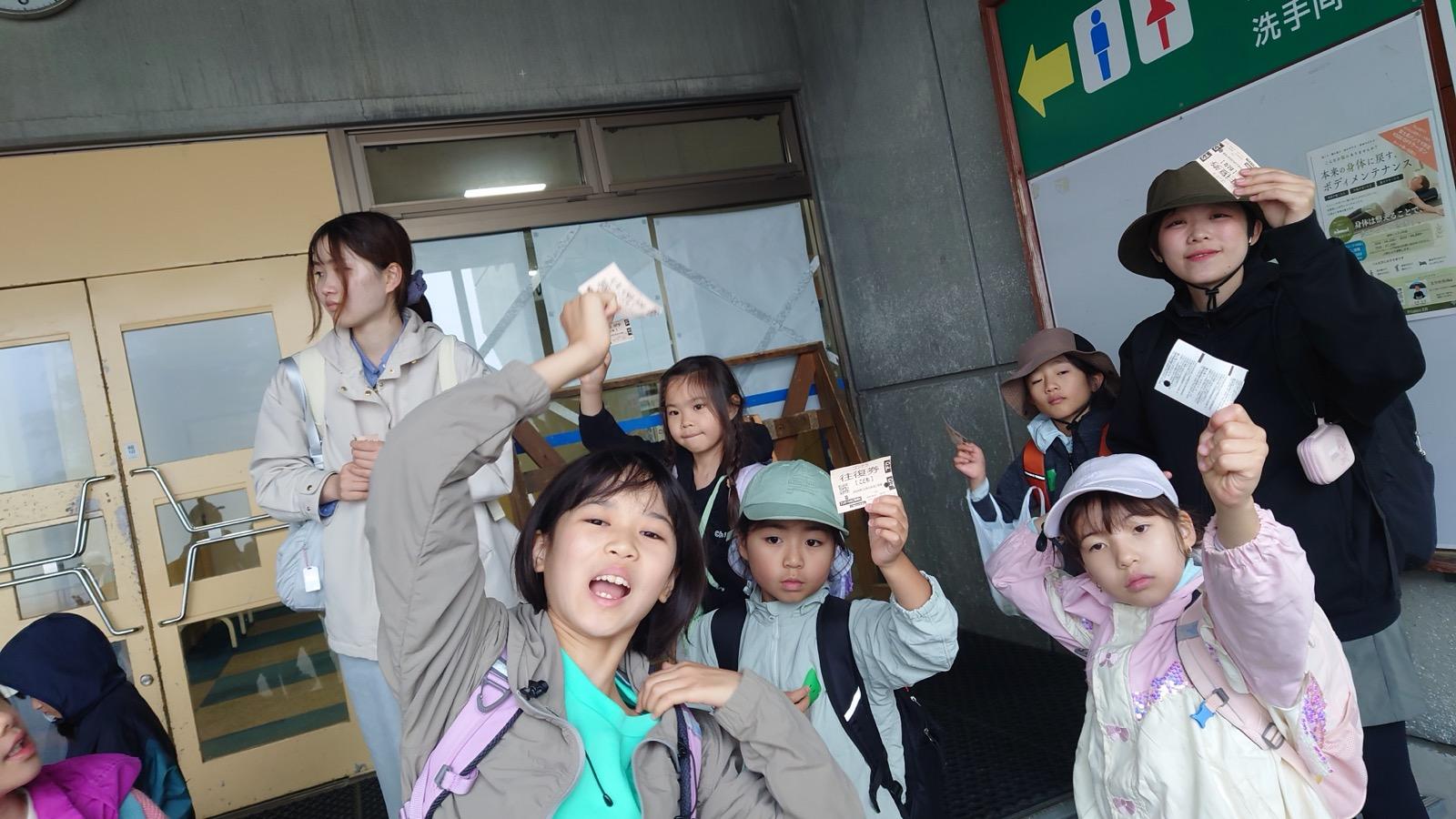 ゴンドラ山頂駅の建物前。子どもたちが往復券を手に持って掲げ、カメラに向かっている