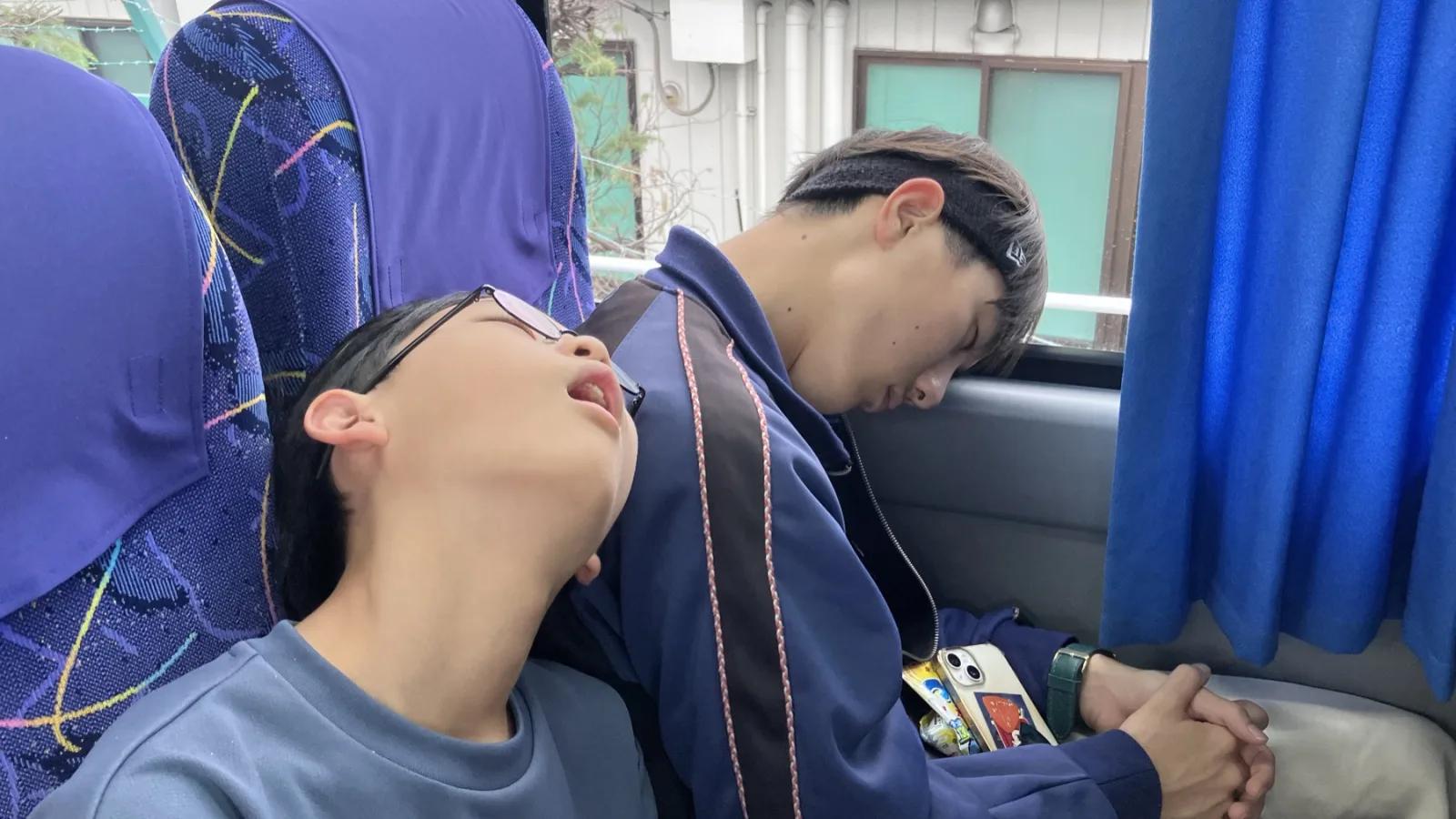バスの車内。座席で口を開けて眠り込んでいる参加者と、隣で首を落として眠っている参加者