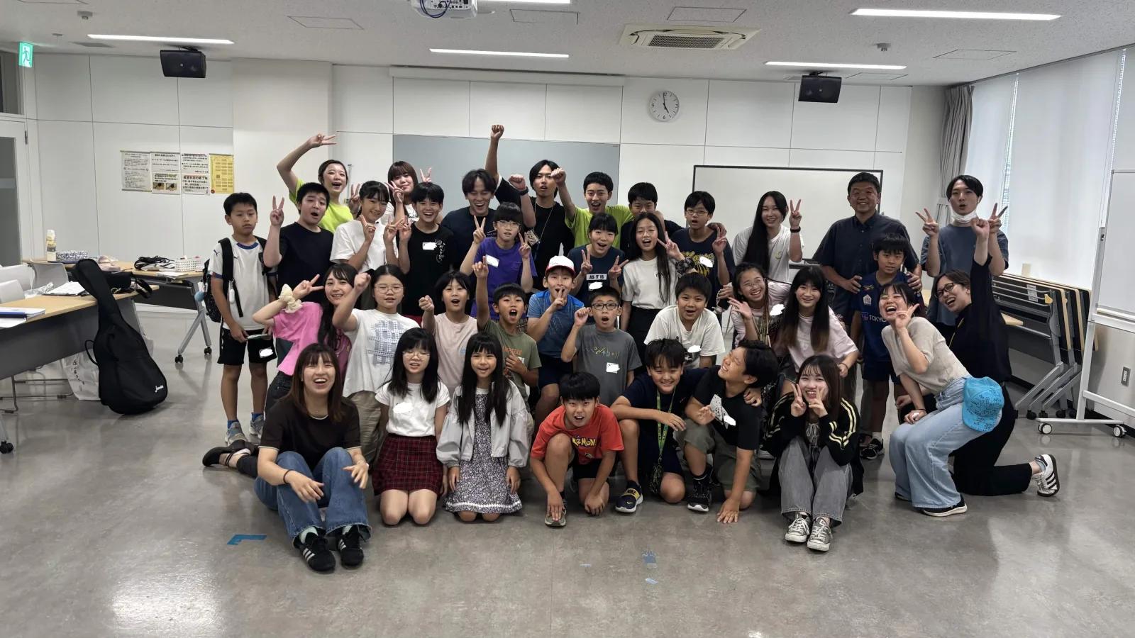 事後集会の会場に参加した子どもたちとリーダー全員が集まり、手を挙げたりピースをしたりして記念撮影をしている